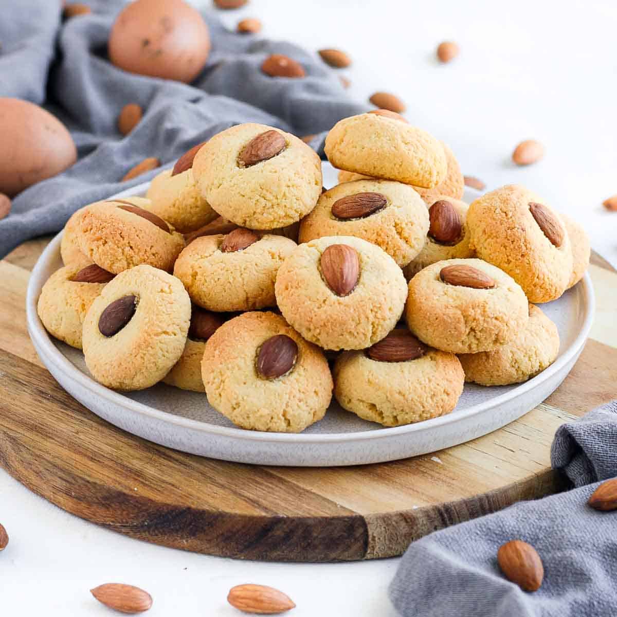 Stack of almond cookies on a white plate over a wooden board.