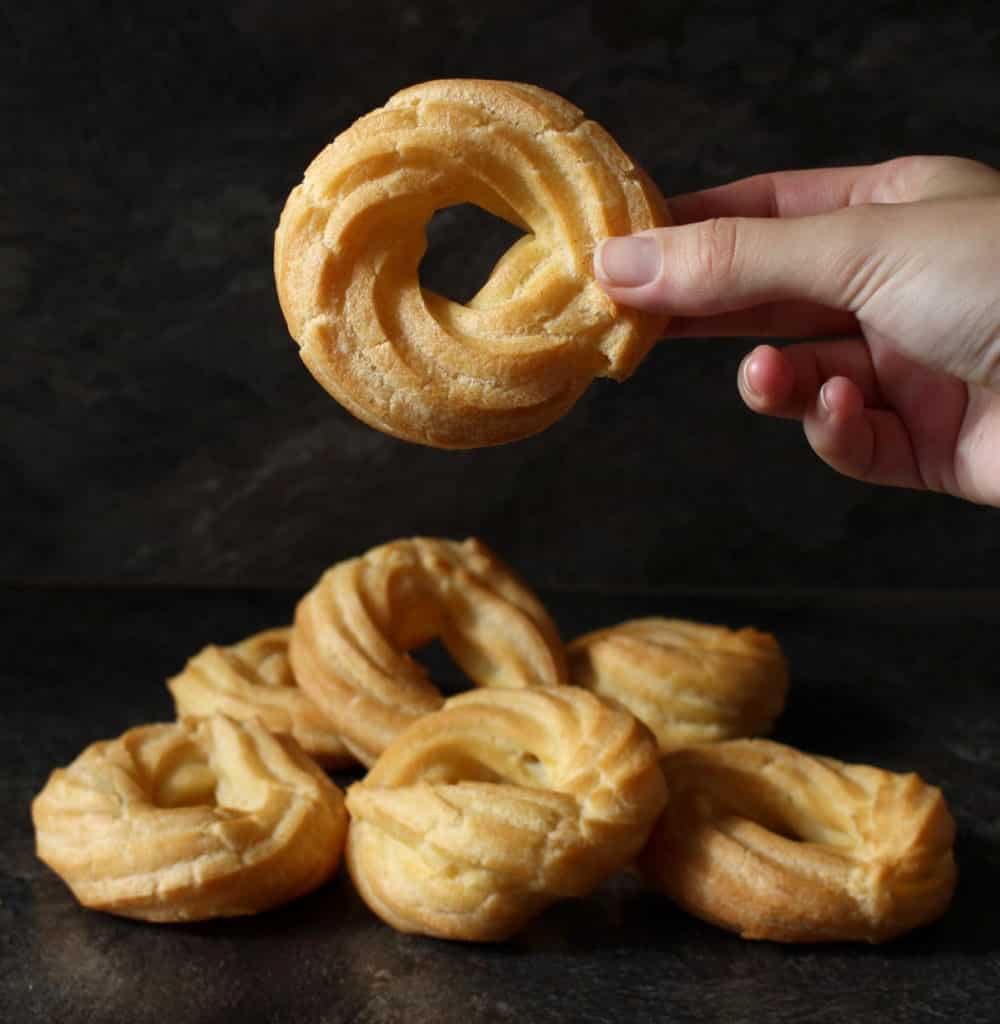 Holding one cruller donut over a stack of donuts