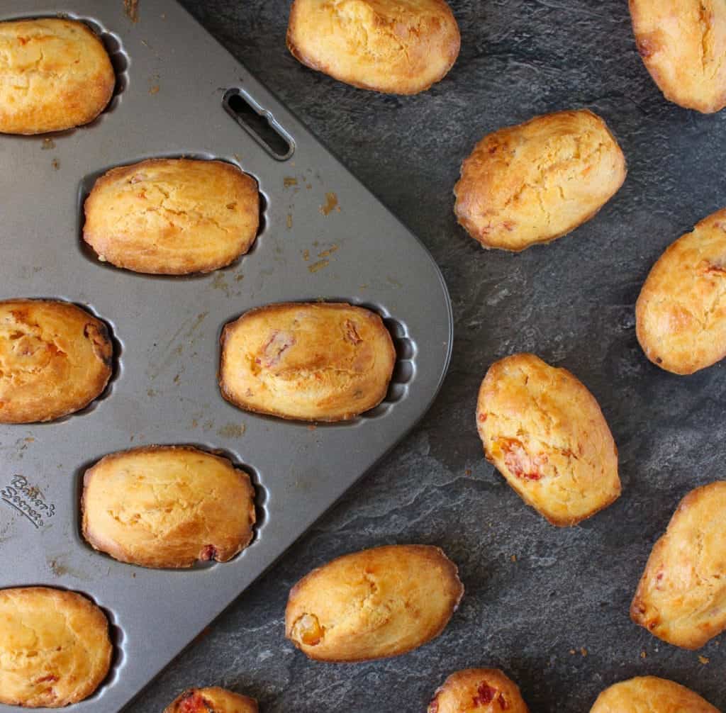 Tomato Madeleines in the pan and over a grey surface.