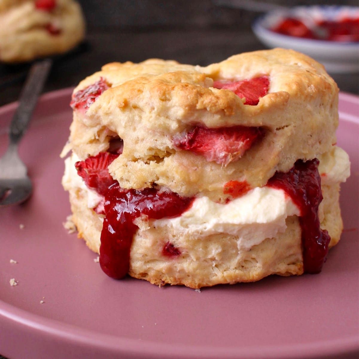 One scone filled with cream and jam over a pink plate