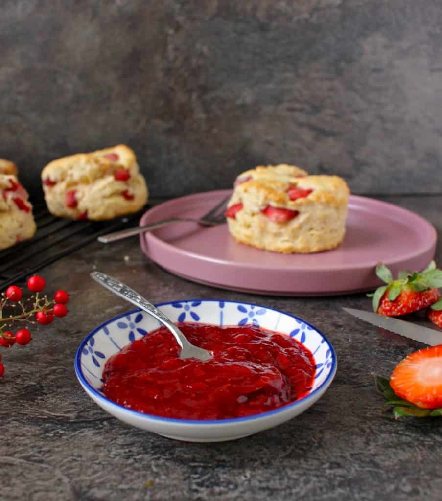 Strawberry Jam in a small bowl with scones in the background 