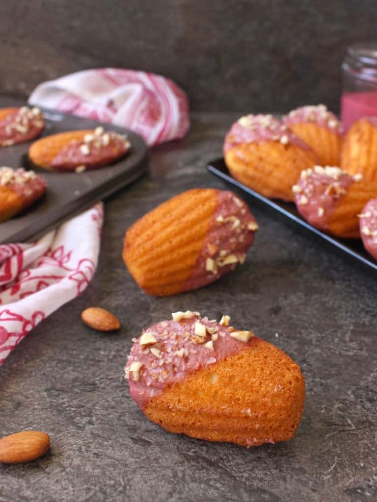 One madeleine on its side on a grey surface with almonds.