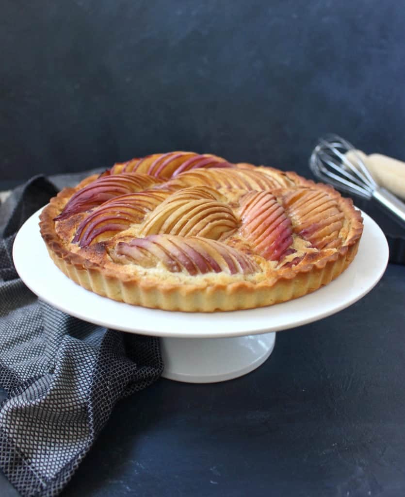 Tart on a white cake stand against a black surface.