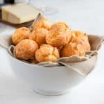 Cheese puffs in a white bowl over a beige napkin.