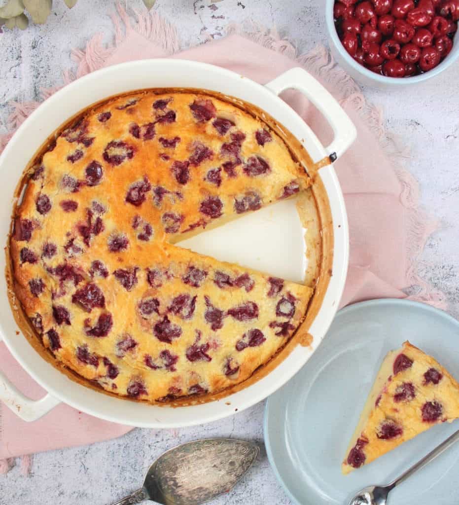 Clafoutis in a round ceramic dish with one slice placed on a blue plate