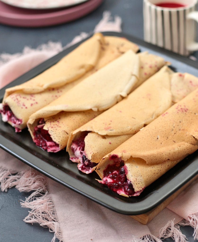 Crepes filled with a berry compote on a black plate.