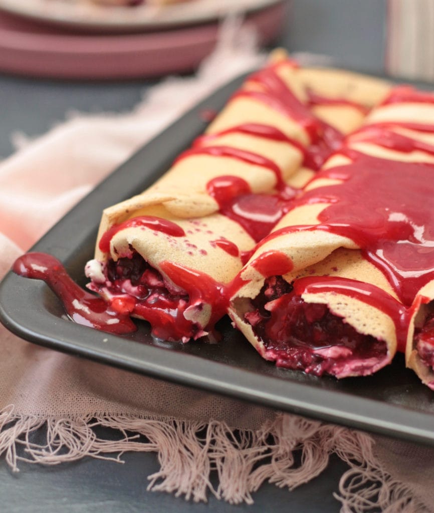 Crepes rolled on a black plate and covered with a Raspberry Coulis.