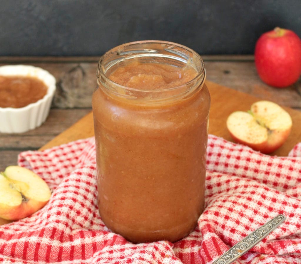 Apple sauce in a glass jar over a red and white tea towel