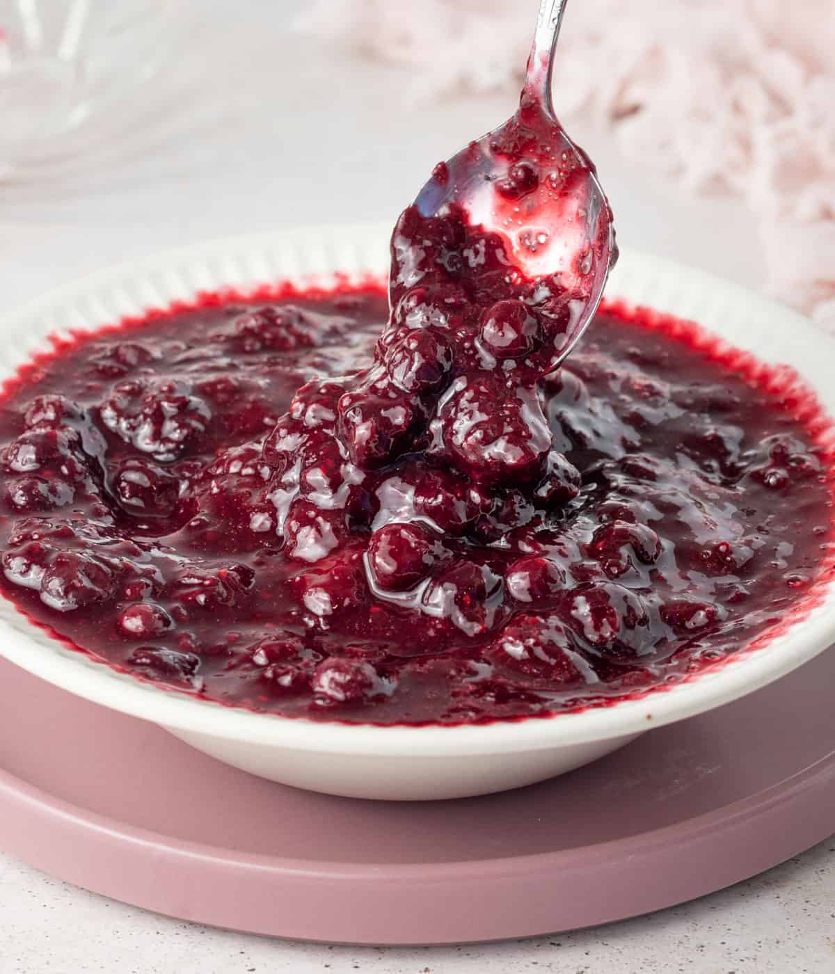 Close up on the compote dripping from a silver spoon into a bowl.