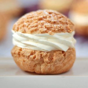 Close up on a choux bun filled with cream over a beige plate