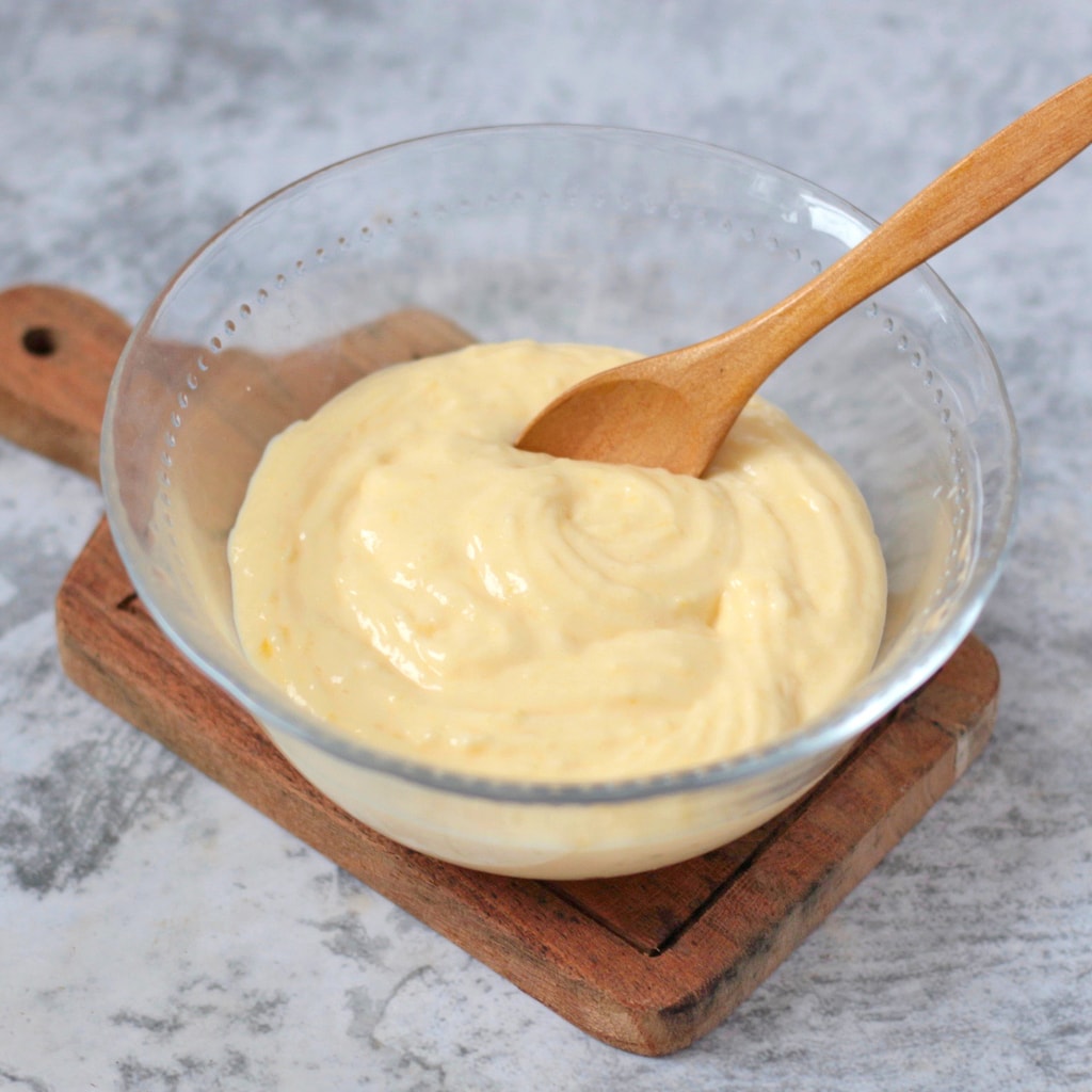 Creme Patissiere in a glass bowl with a wooden spoon.