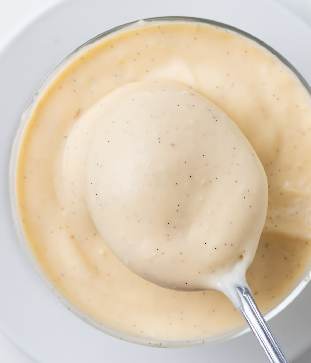 Custard on a spoon over a bowl filled with cream seen from above.