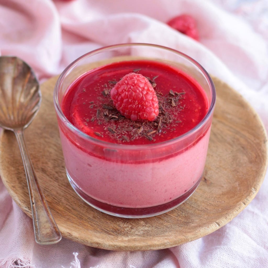 Close up on a Mousse Cup with chocolate shavings and a fresh raspberry, placed over a wooden plate.