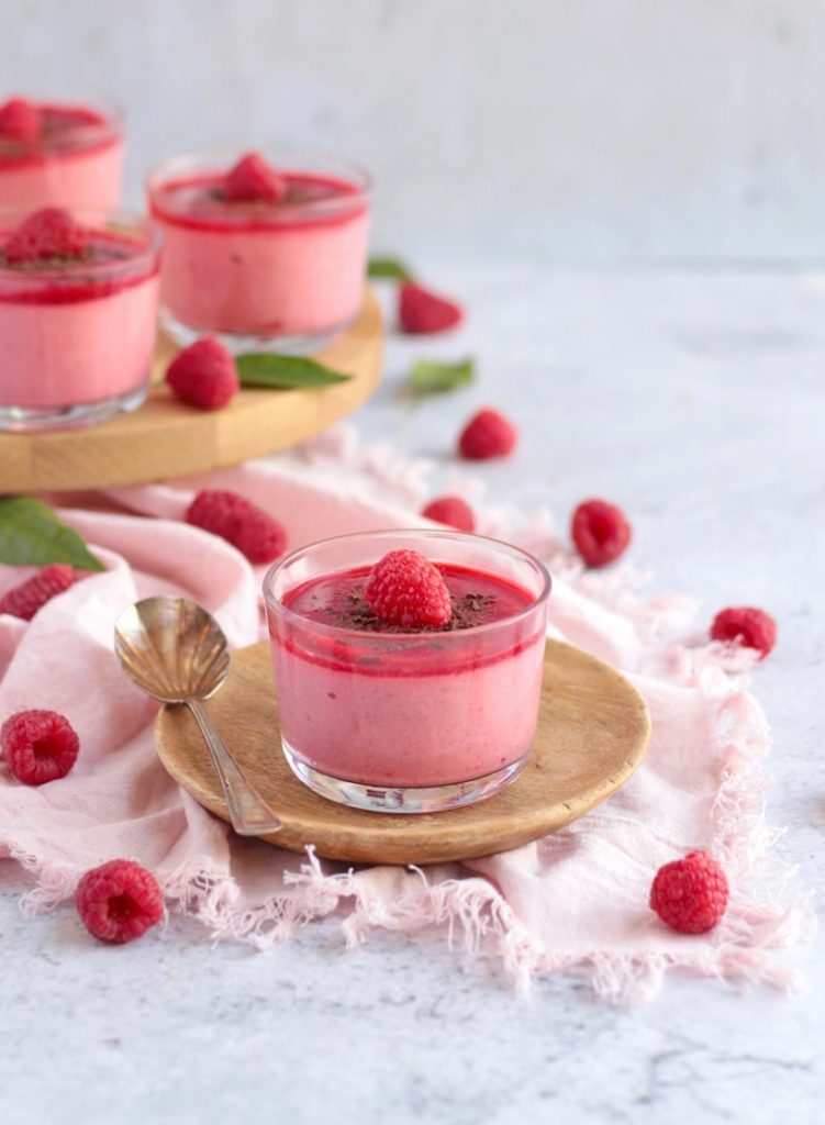 One Raspberry Mousse Cup on a plate surrounded by fresh raspberries.