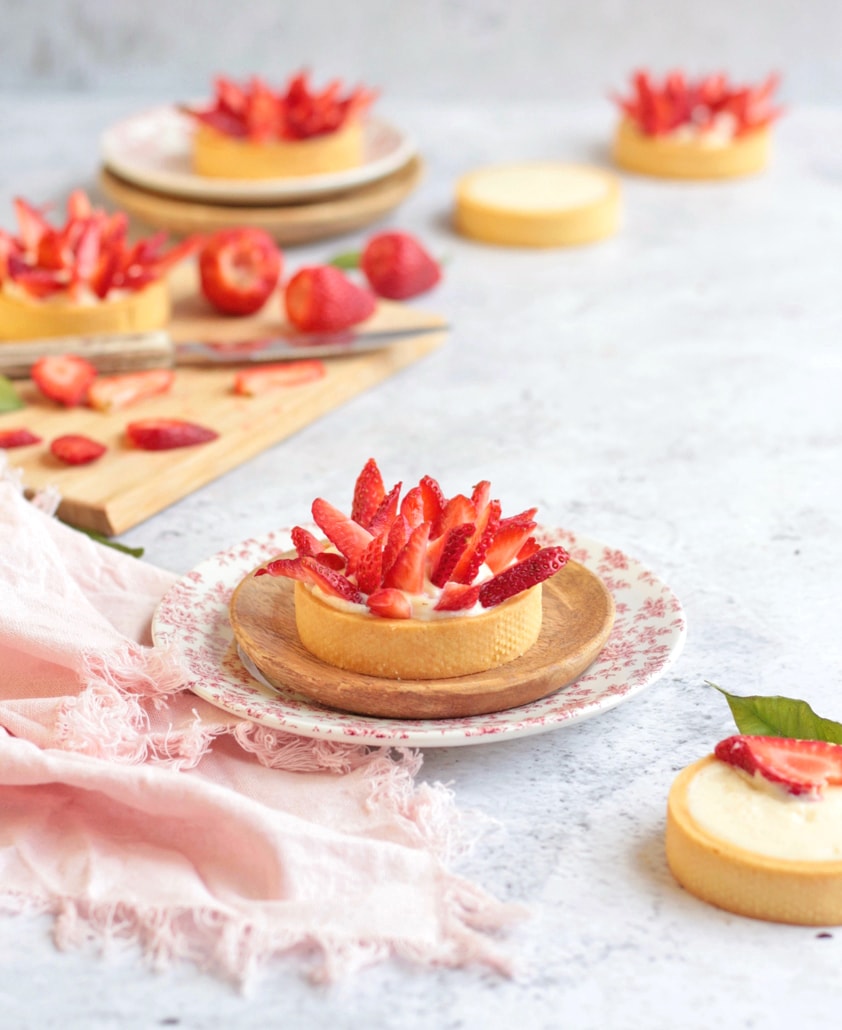 Small Strawberry Tart on a plate with a pink napkin and a wooden cutting board with strawberries in the background