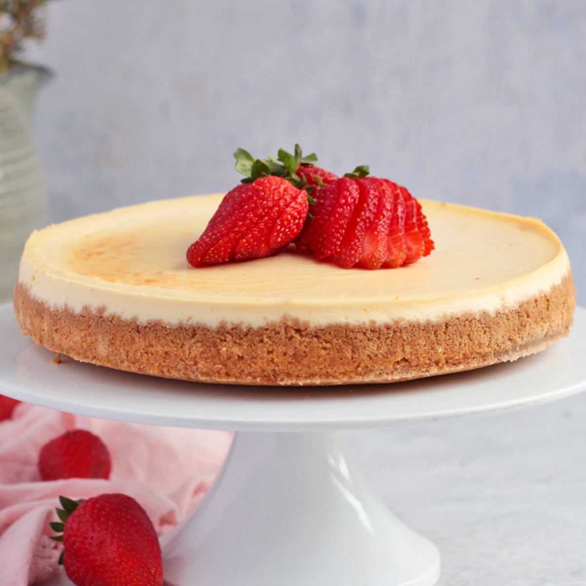 Cheesecake on a white cake stand topped with strawberries