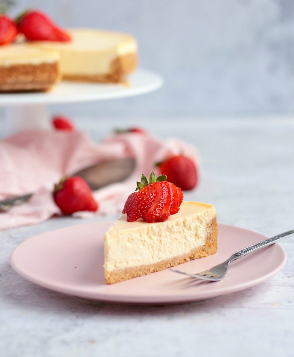 One slice of cheesecake topped with fresh strawberries on a pink plate
