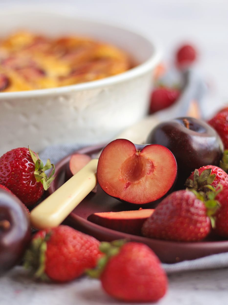 Photo of a plum sliced in half, surrounded by strawberries and plums