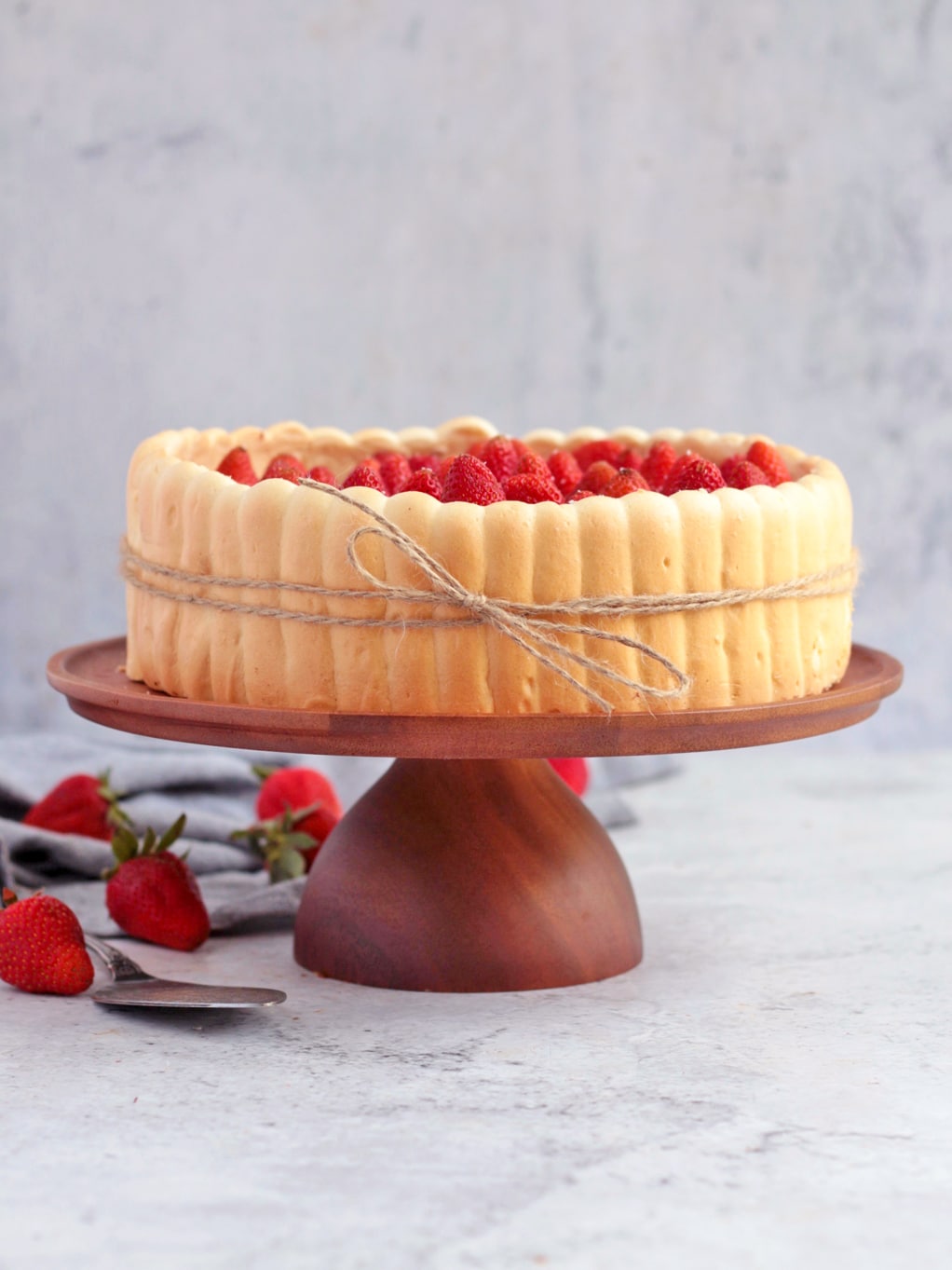 Finished cake on a wooden cake stand surrounded by strawberries