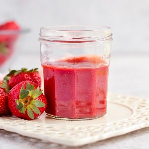 Strawberry Coulis in a Glass Jar surrounded by fresh strawberries