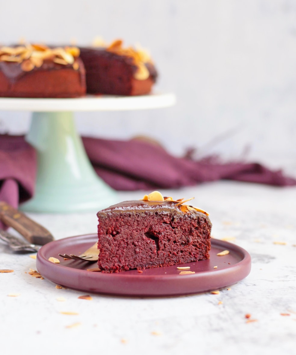 A slice of cake on a purple plate with the cake in the background