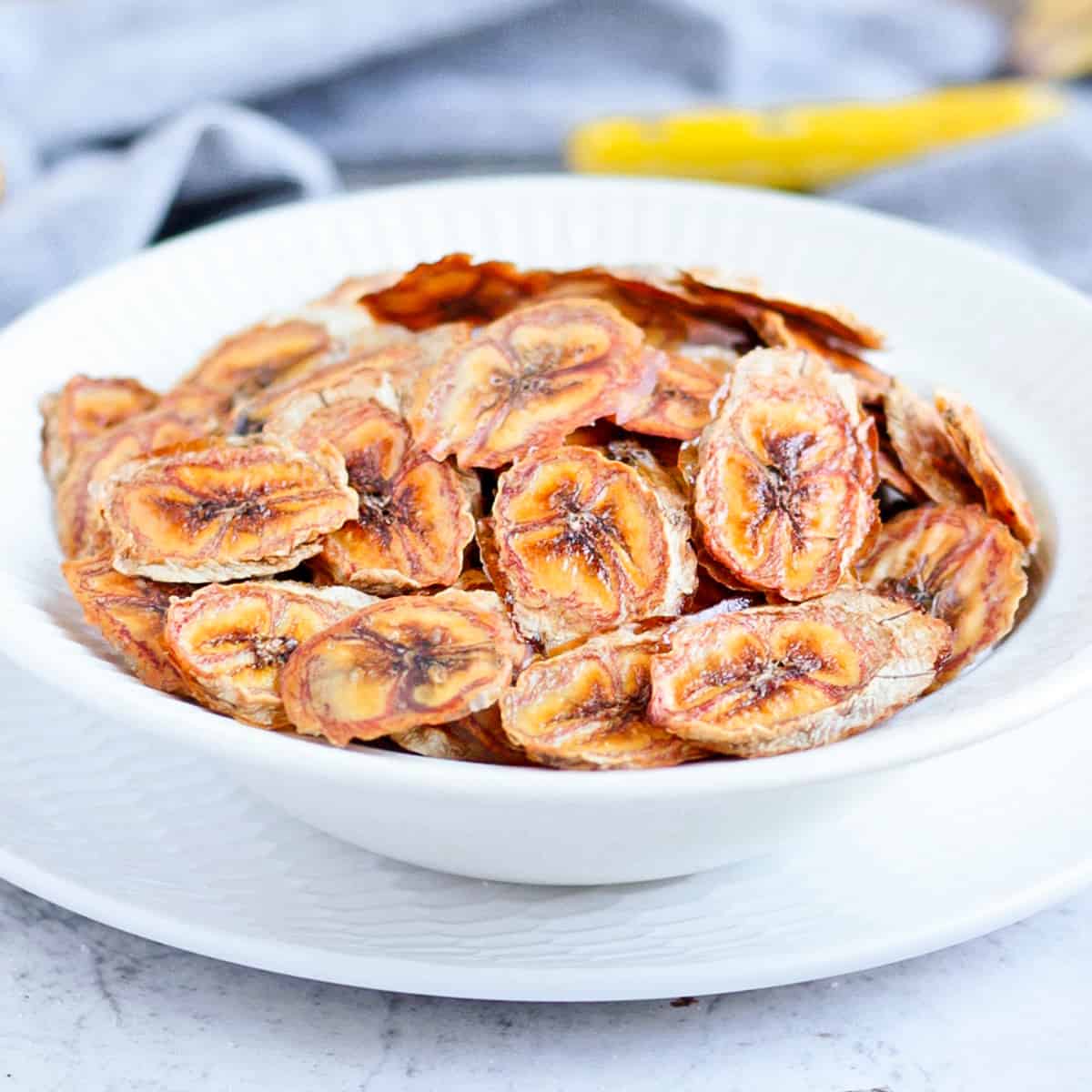 Fruit Chips in a white bowl surrounded by lemons an a banana.