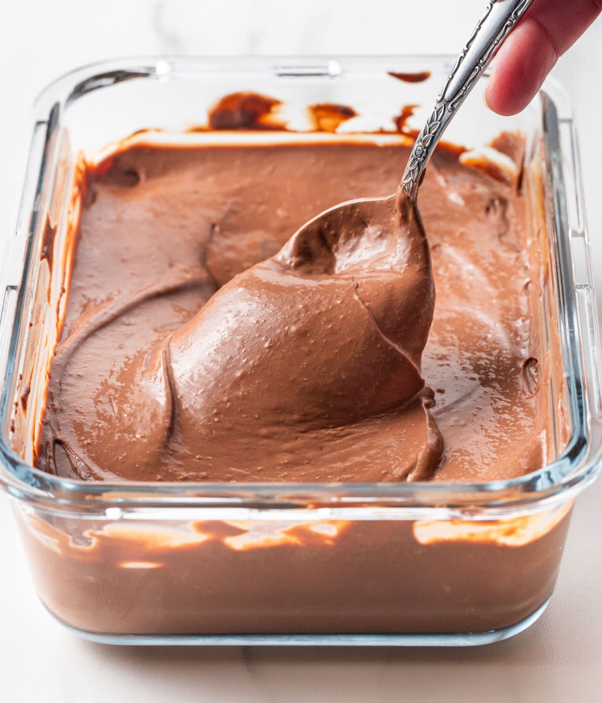 Cream falling off a spoon inside a glass container.