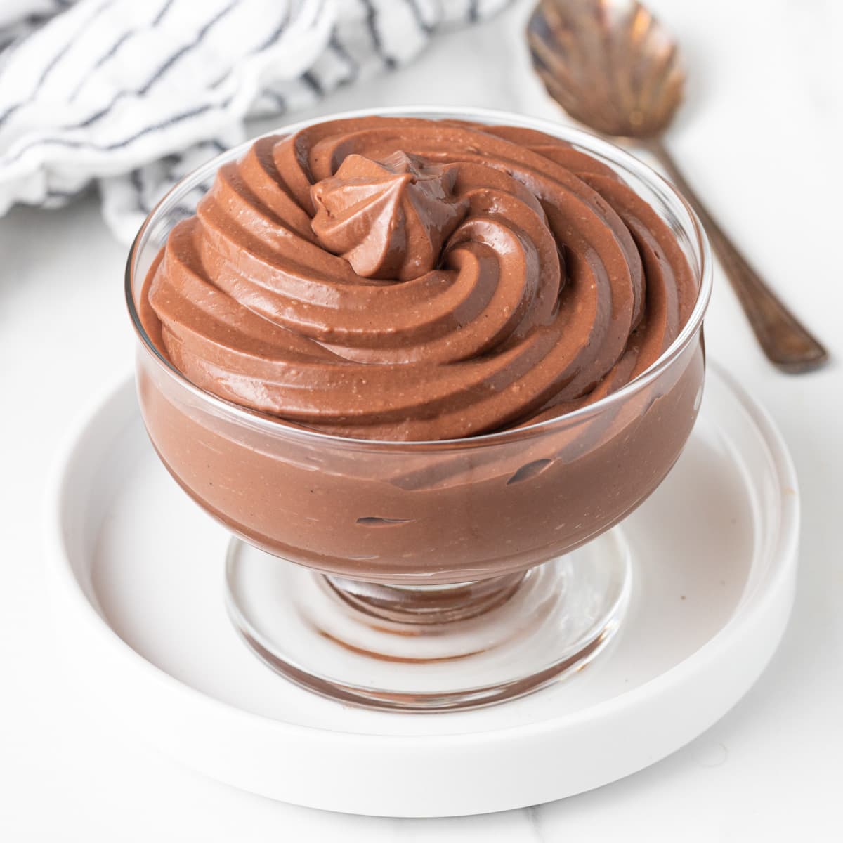 Chocolate cream piped inside a serving cup with a tea towel a spoon in the background.