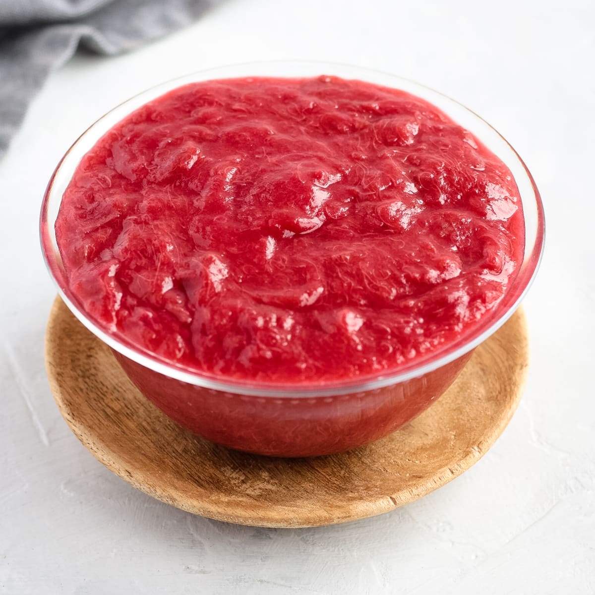 Stewed Rhubarb in a glass bowl over a wooden plate