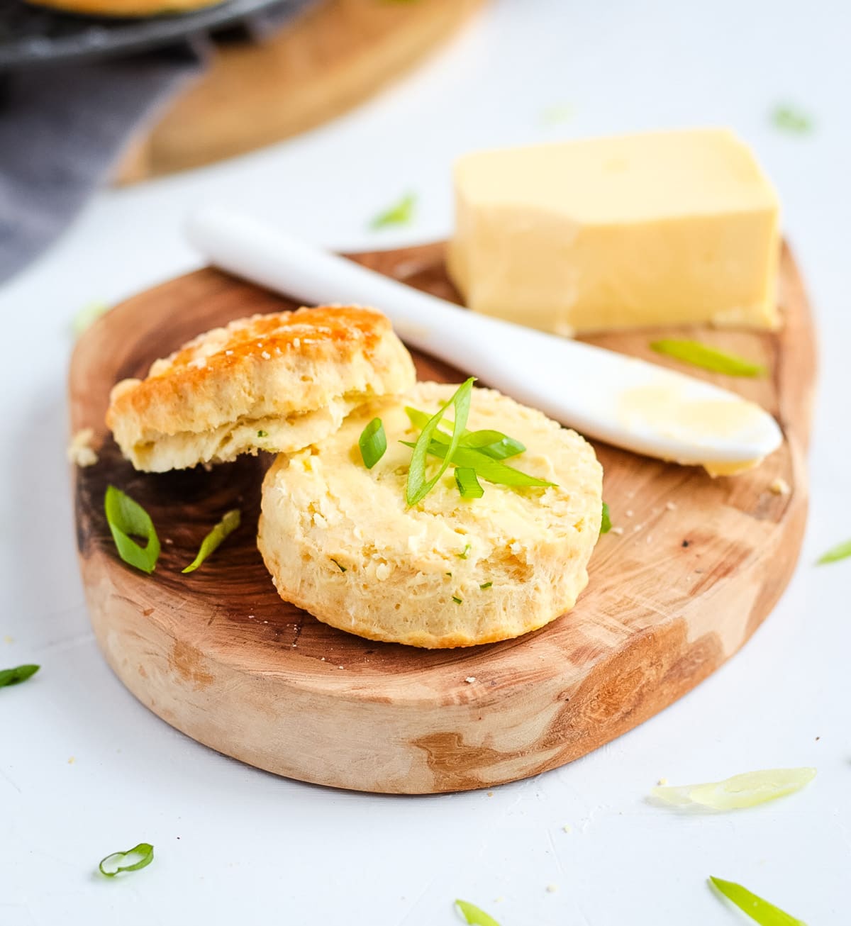 Scone sliced in half with butter and fresh sliced spring onion, over a wooden tray