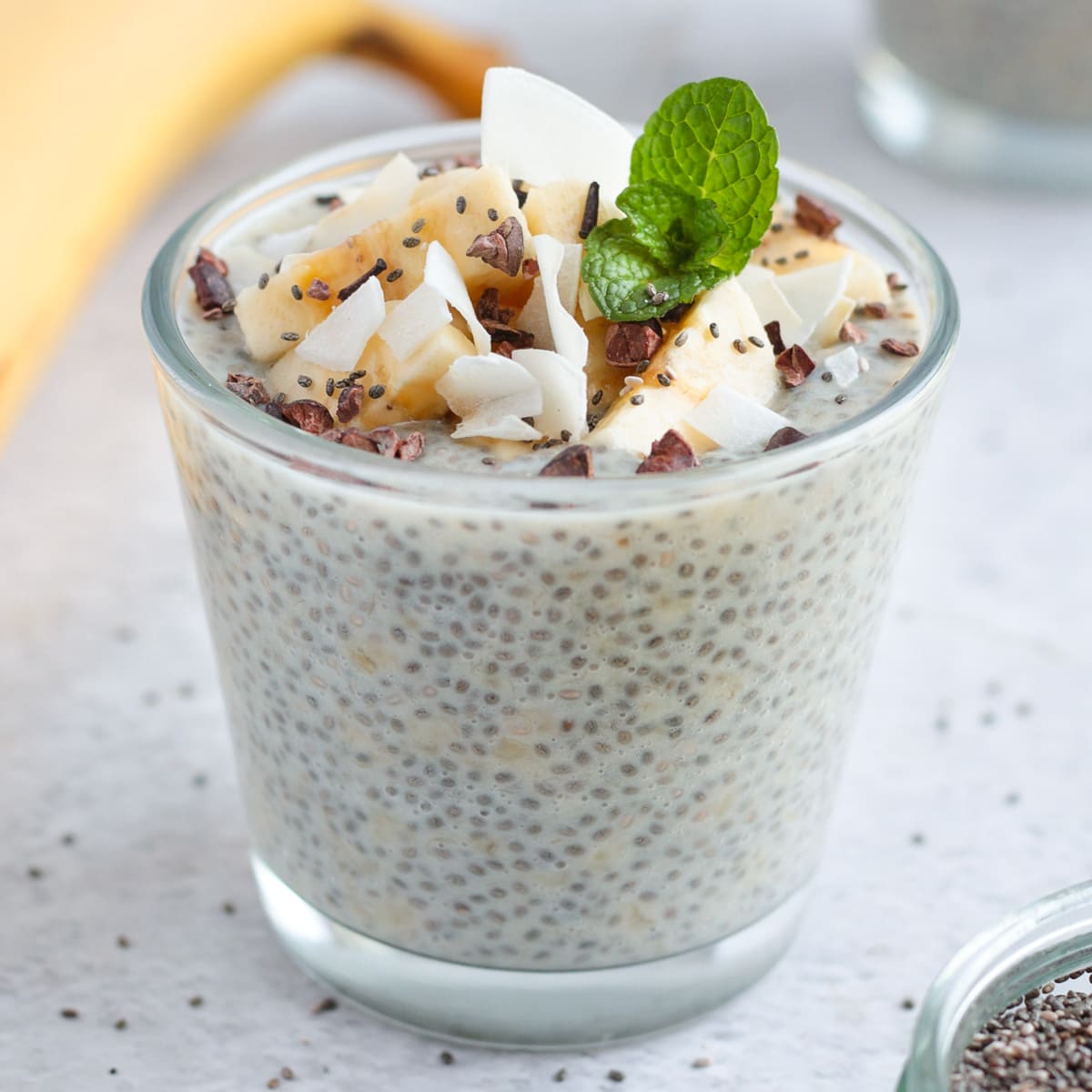 Banana Chia Seed Pudding in a small glass cup topped with coconut, bananas and mint