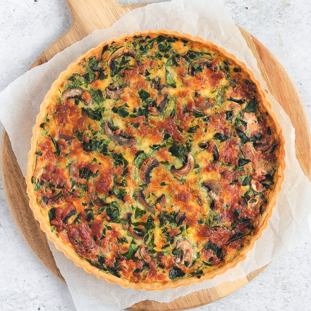 Flatlay of the quiche over white baking paper on a round wooden board