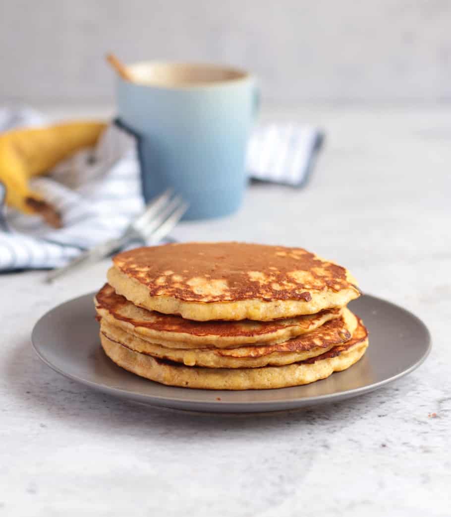 Four large pancakes on a grey plate behind a white background.