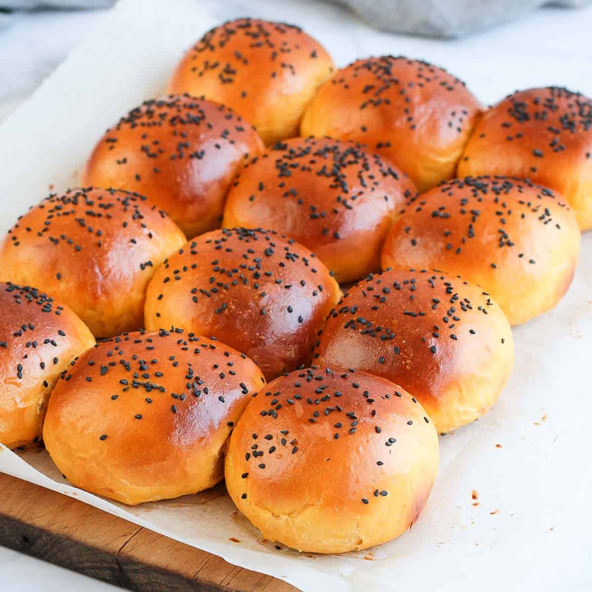 Buns on a sheet of baking paper over a wooden cutting board.