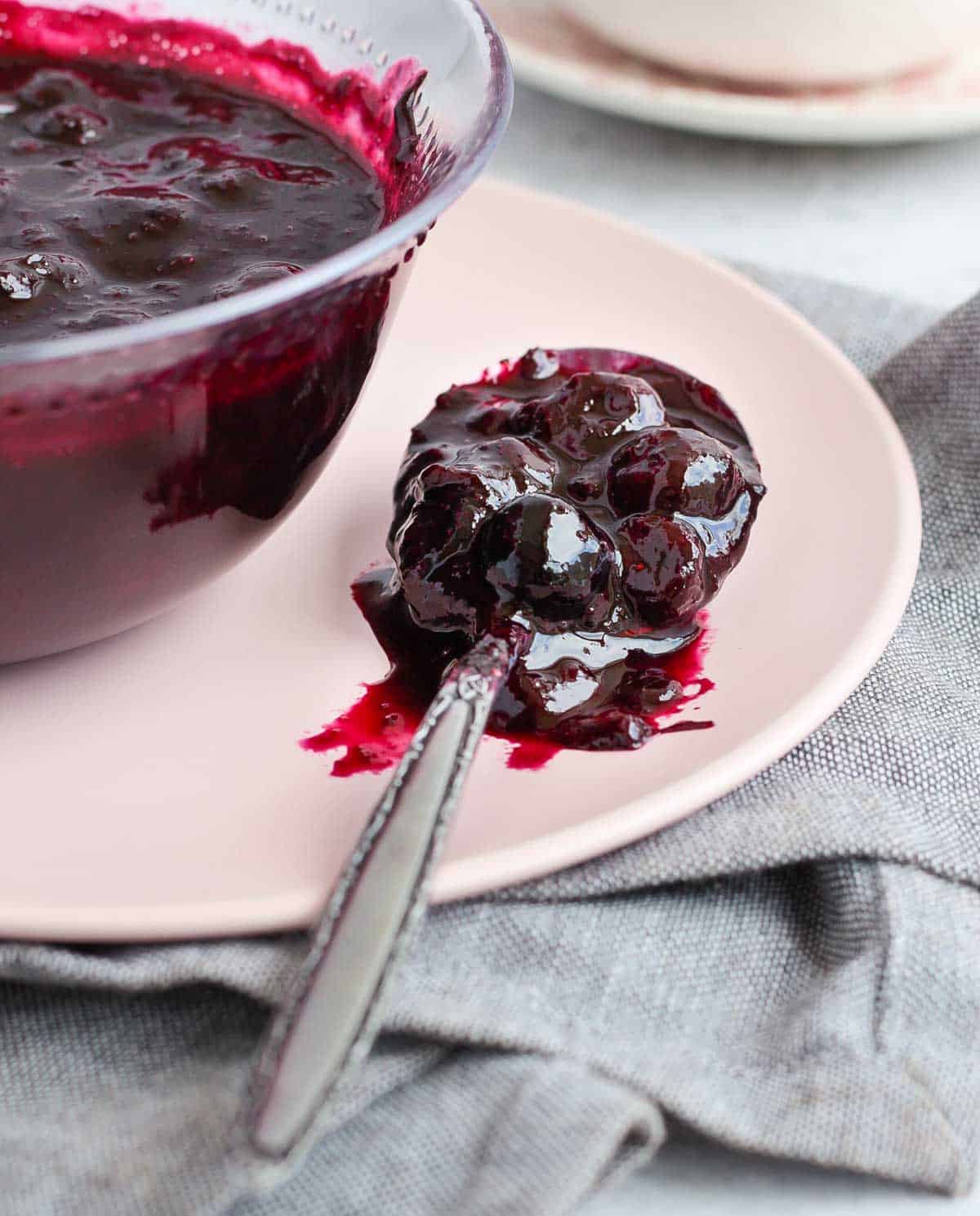 A spoon full of compote over a pink plate.