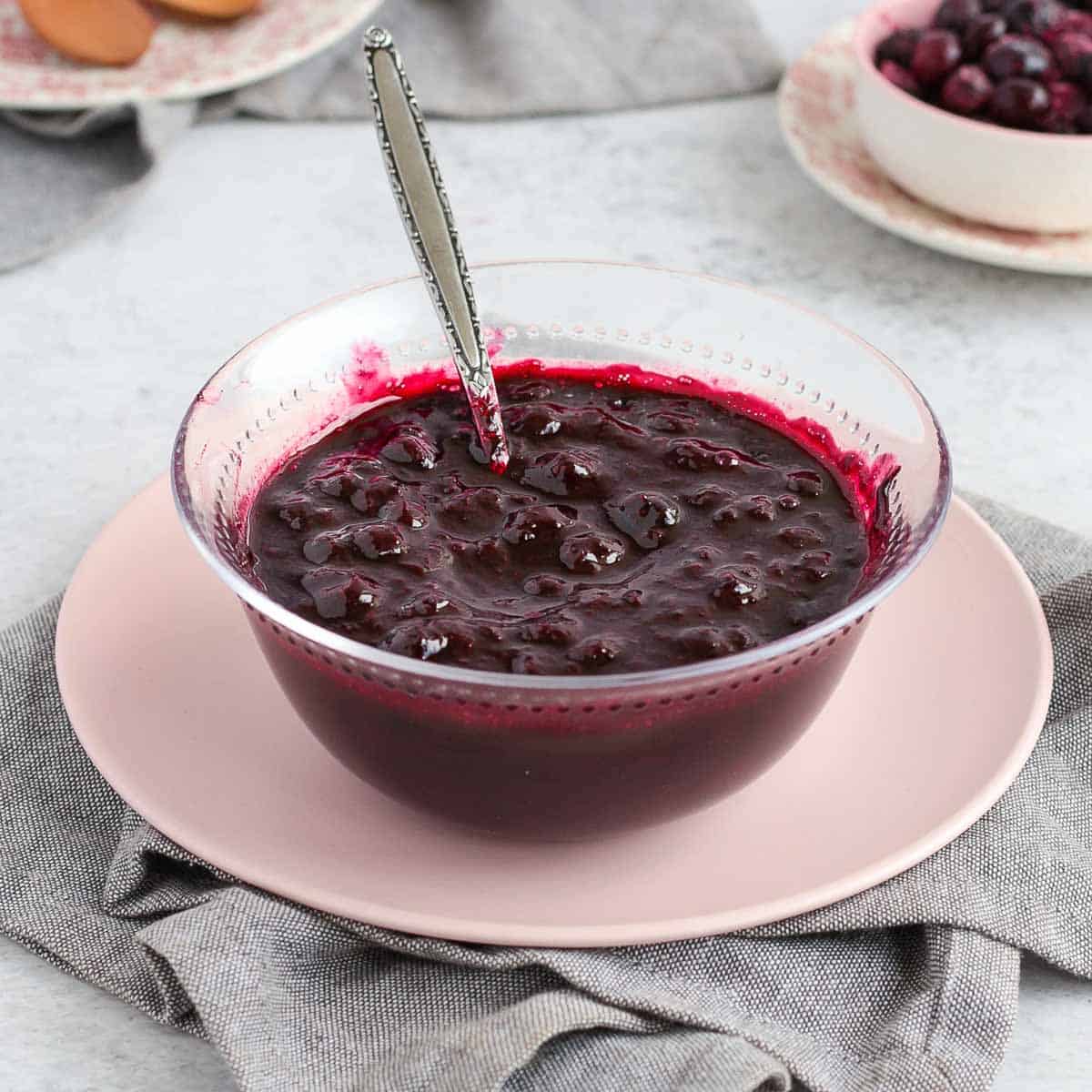 Blueberry Compote in a glass bowl over a pink plate.