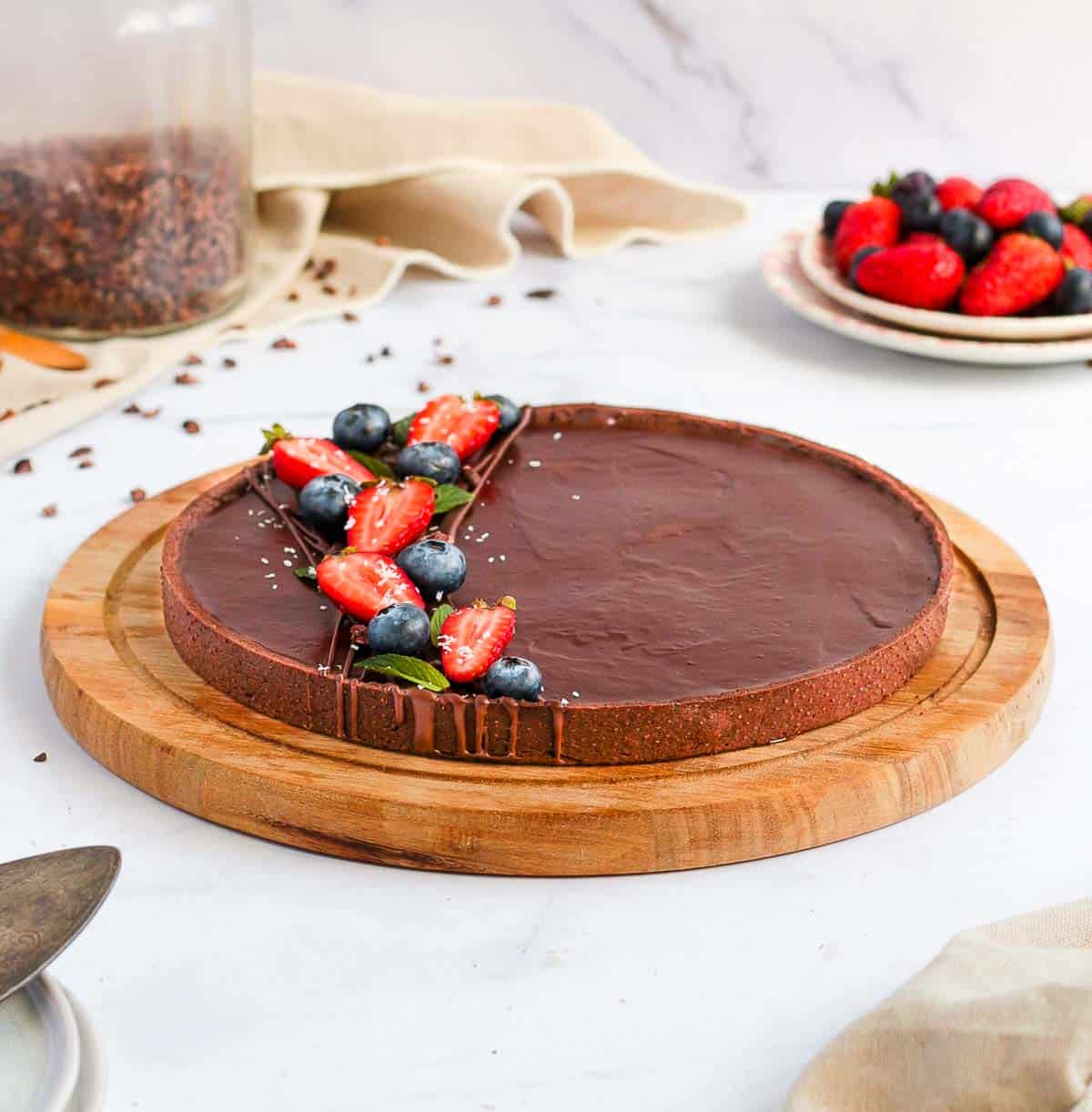 Chocolate Tart on a round wooden board over a white surface.