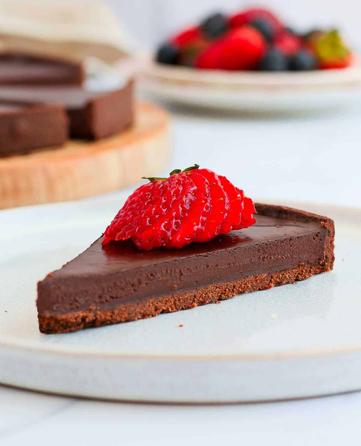 A slice of chocolate ganache tart topped with a strawberry on a white plate.