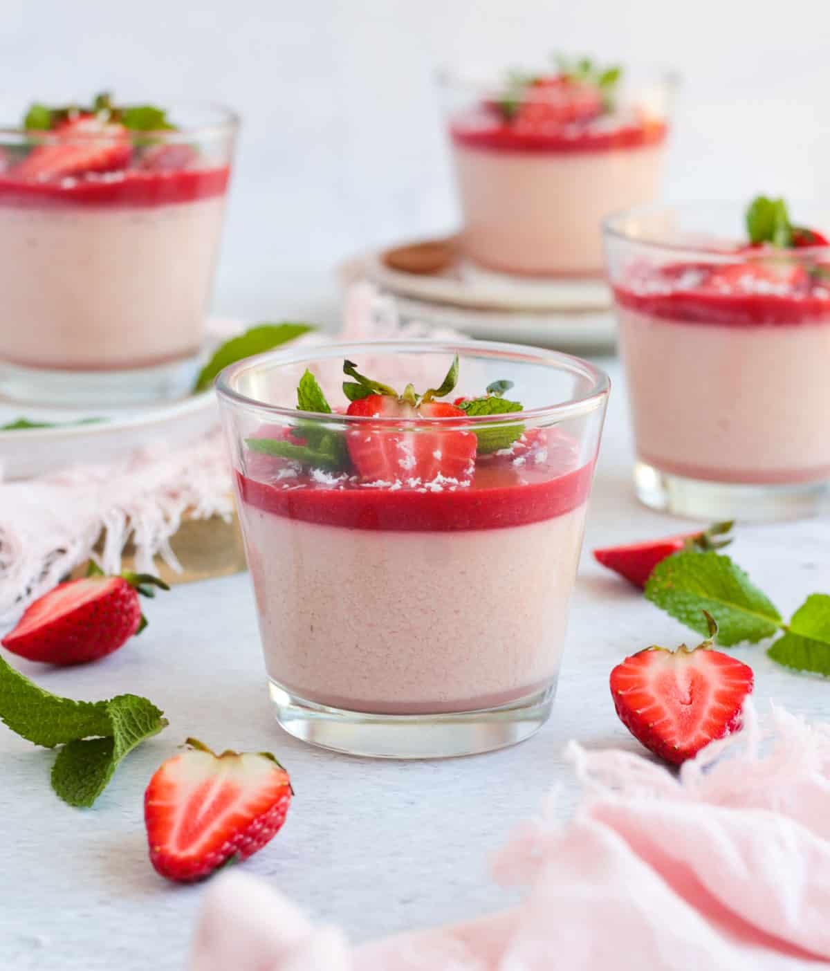 four cups of panna cotta surrounded by fresh strawberries and pink napkins.