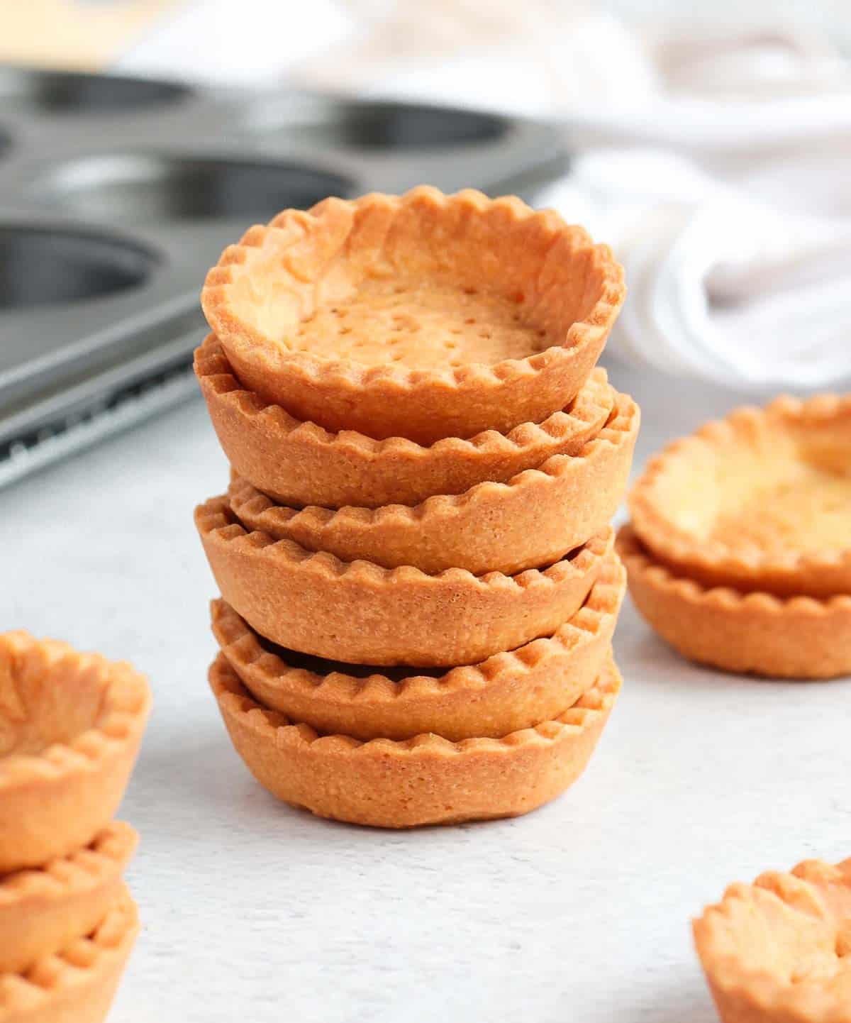 Mini tart shells stacked on a grey surface.