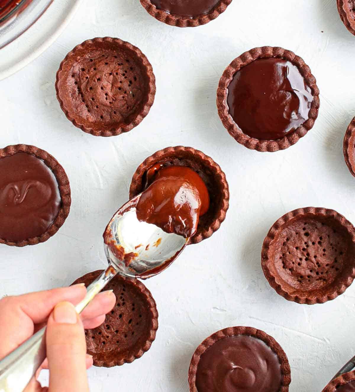 Pouring the chocolate ganache inside the tartlet shells.