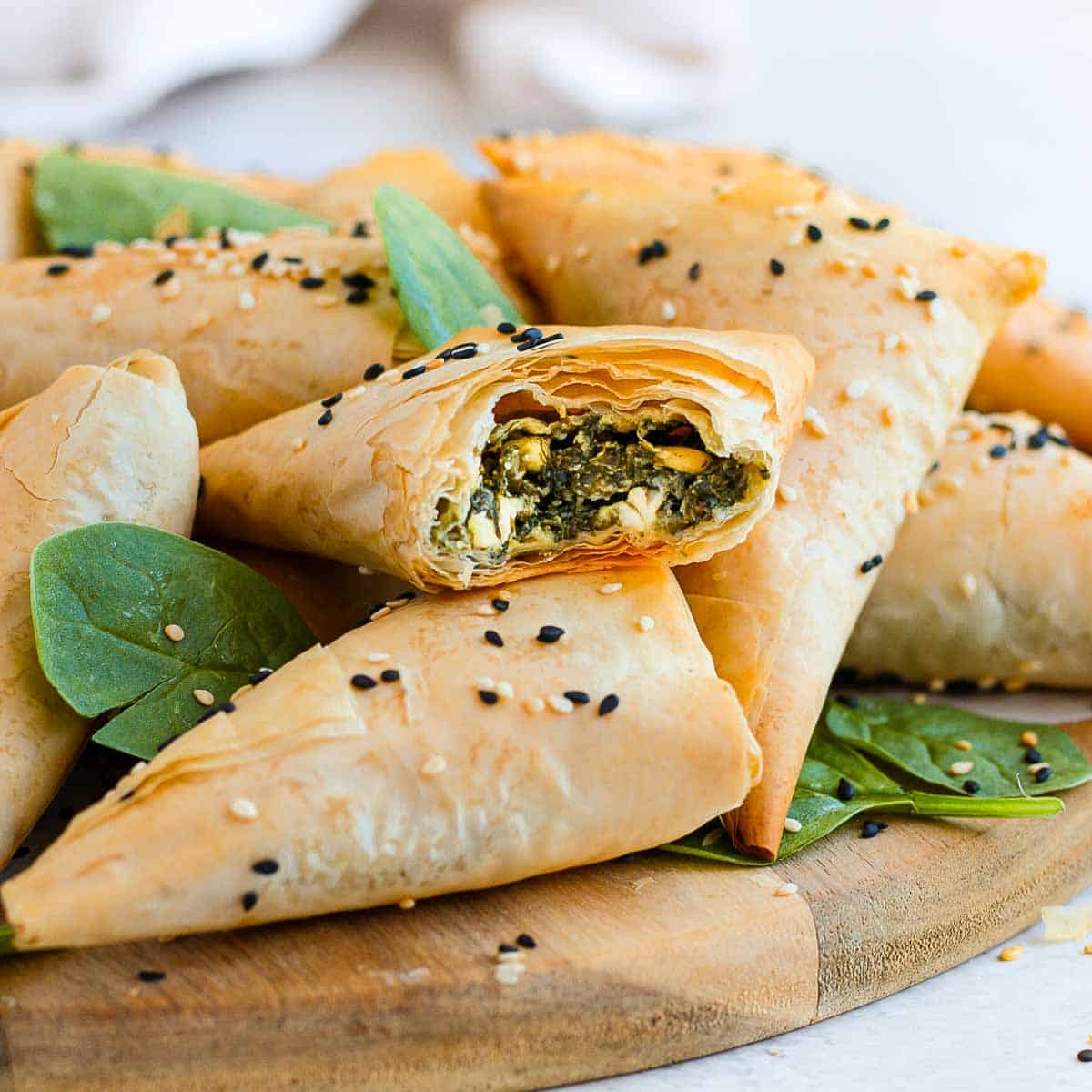 One spanakopita pastry cut in half placed over other pastries.