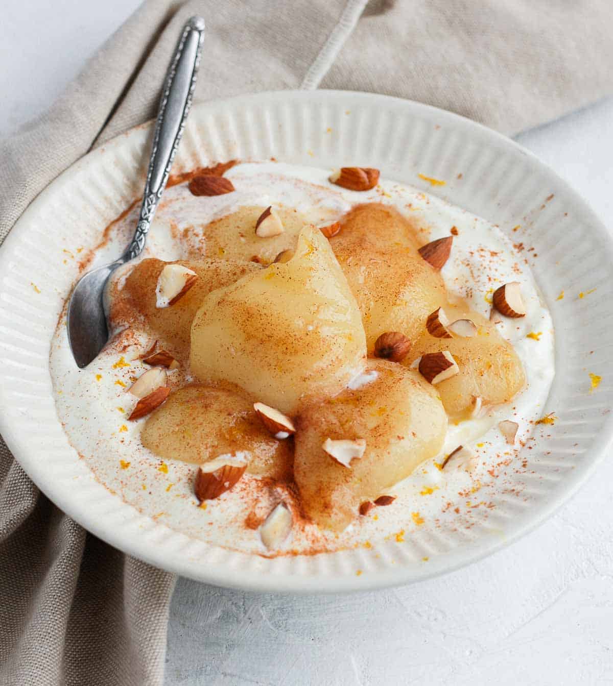 Poached pears over yogurt in a white bowl.