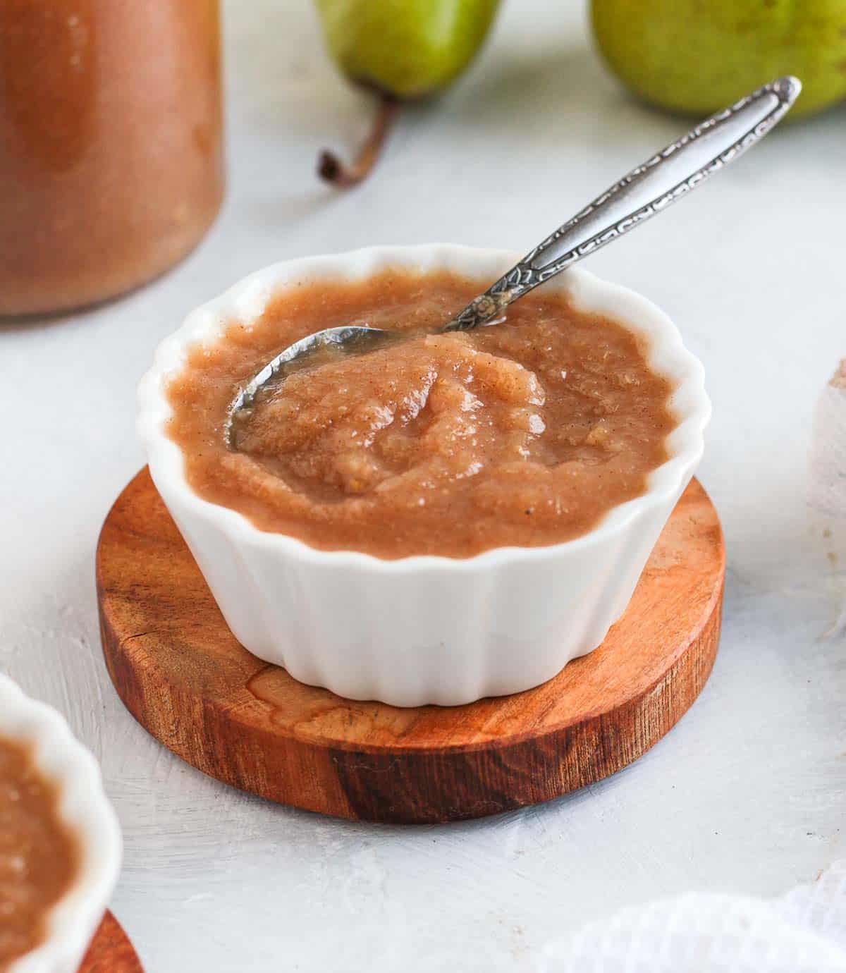 Compote in a small white bowl over a wooden coaster with a silver spoon.