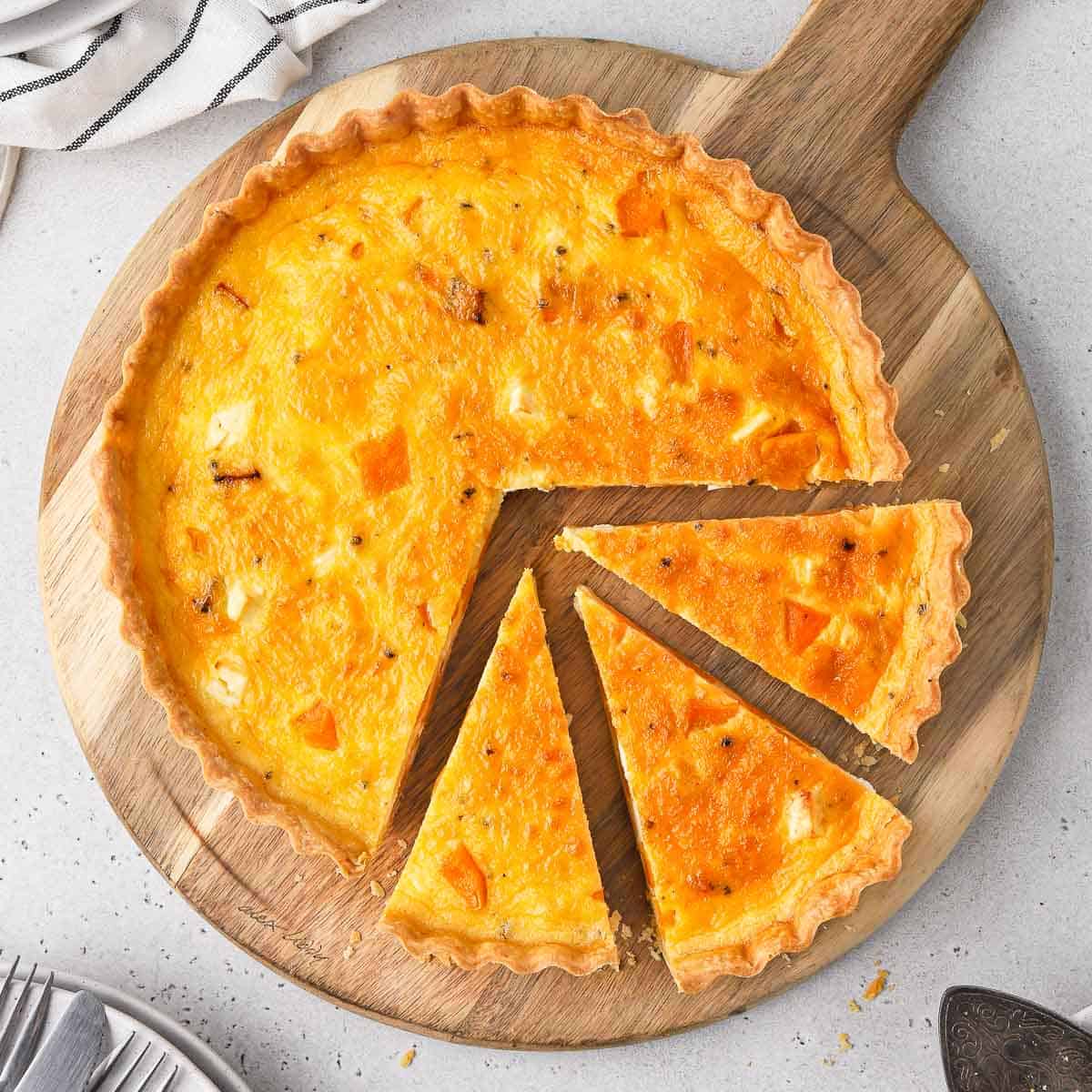 Flatlay of the pumpkin quiche on a wooden board with 3 slices cut off.