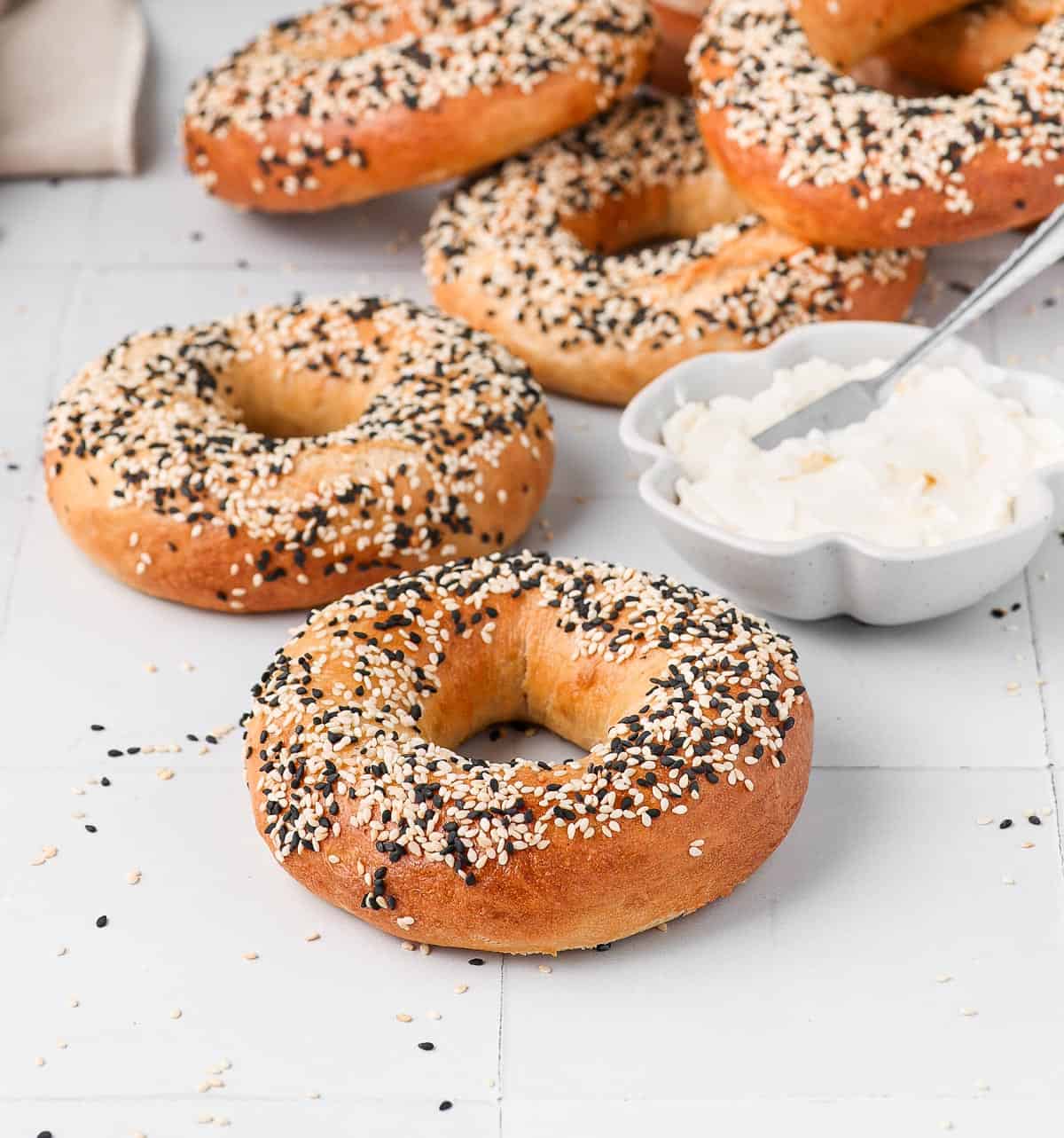 Bagels on a white surface with a bowl of cream cheese.