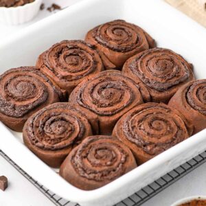 Side view on the chocolate cinnamon rolls in a white baking dish.