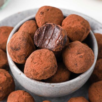 One bite taken off a chocolate truffle stacked inside a small grey bowl.