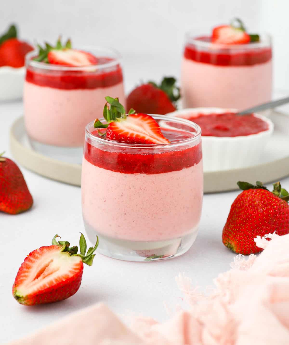 Front view of the dessert in a glass cup surrounded by fresh strawberries.