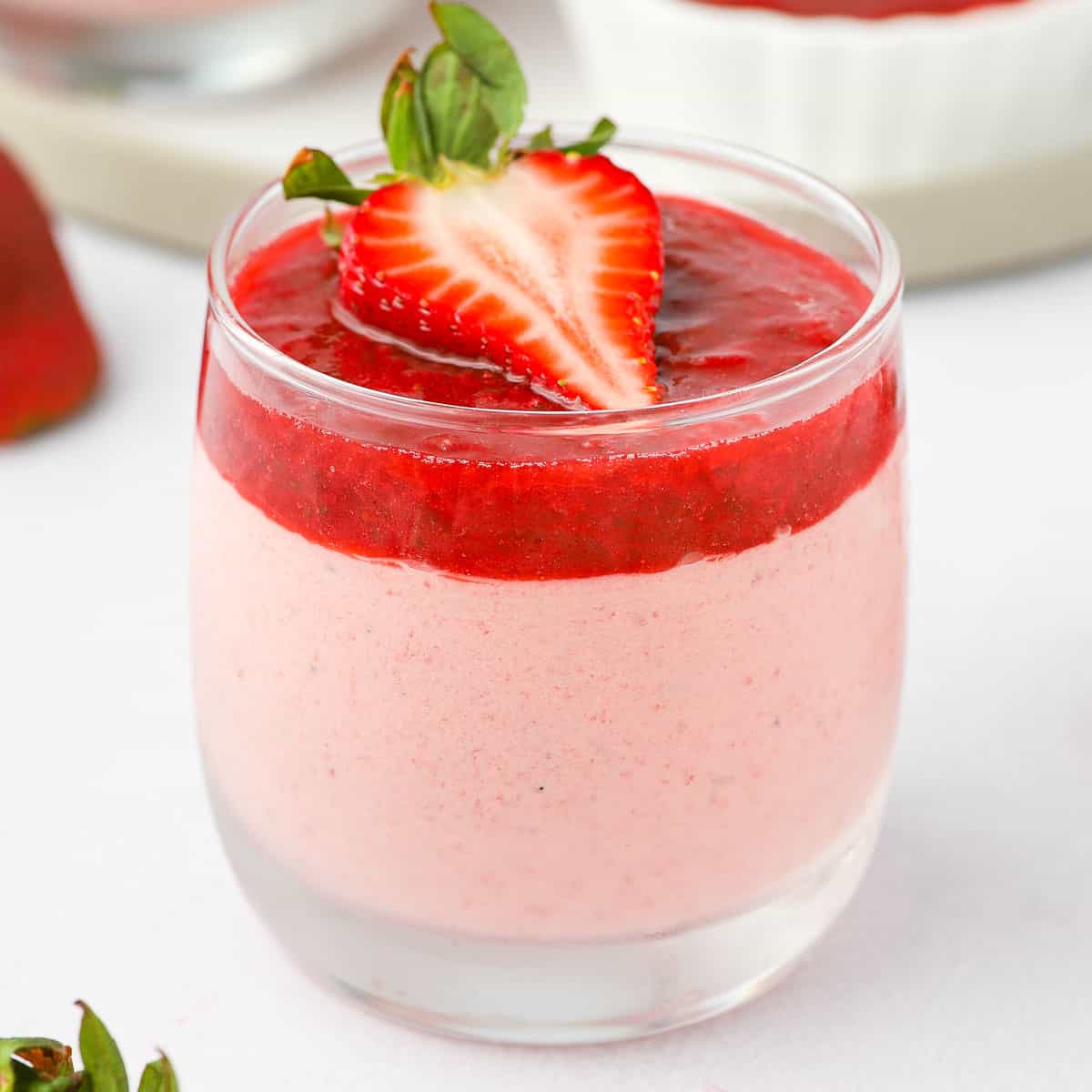 Close up on the strawberry mousse in a glass topped with strawberry compote and half a strawberry.
